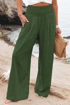 Femme en pantalon large vert, bord de mer, tenant un sac en paille. Mode estivale, tenue décontractée, plage, style bohème chic.