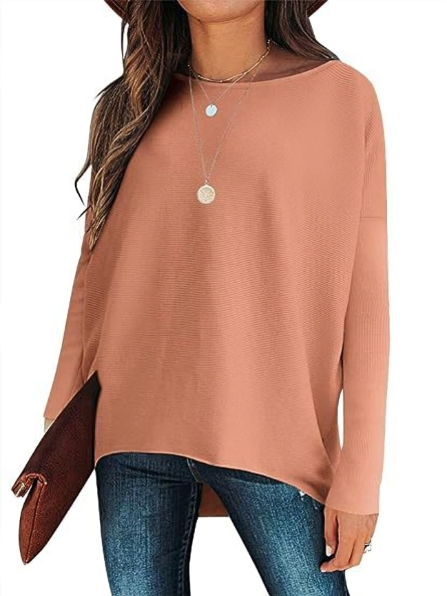 Femme portant un pull oversize rose, jeans bleu, chapeau et collier, tenant une pochette marron. Mode décontractée automne-hiver tendance.