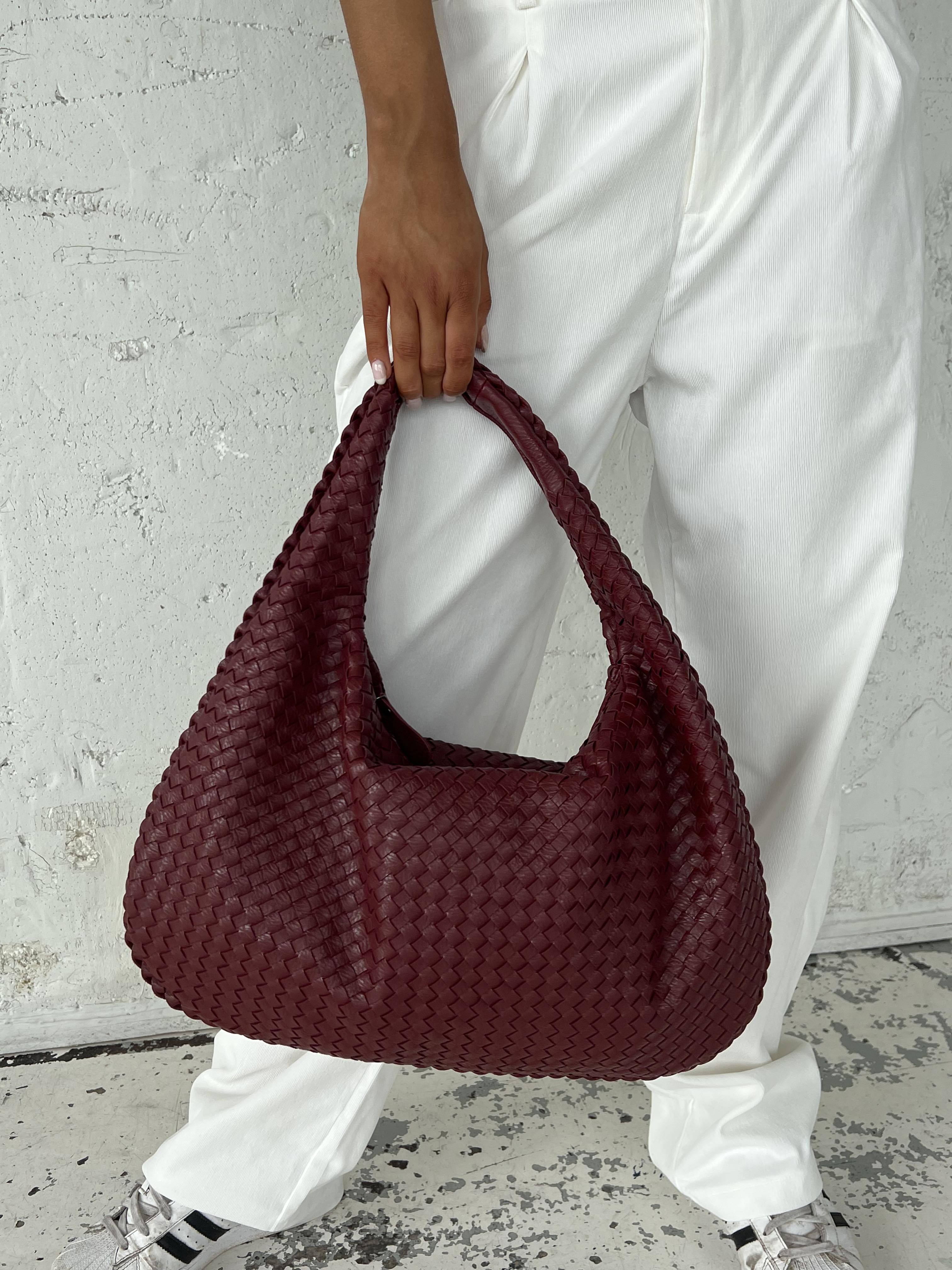 Sac à main tressé bordeaux porté par une personne en pantalon blanc. Accessoire mode élégant, tendance, idéal pour un look chic et moderne.