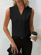 Femme en haut sans manches noir, tenant un café à emporter et une pochette noire, posant devant un mur blanc texturé. Mode élégante et décontractée.