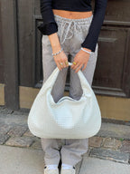 Femme tenant un grand sac à main blanc texturé, portant un pantalon rayé et un haut noir. Mode urbaine, accessoires tendance, style décontracté.