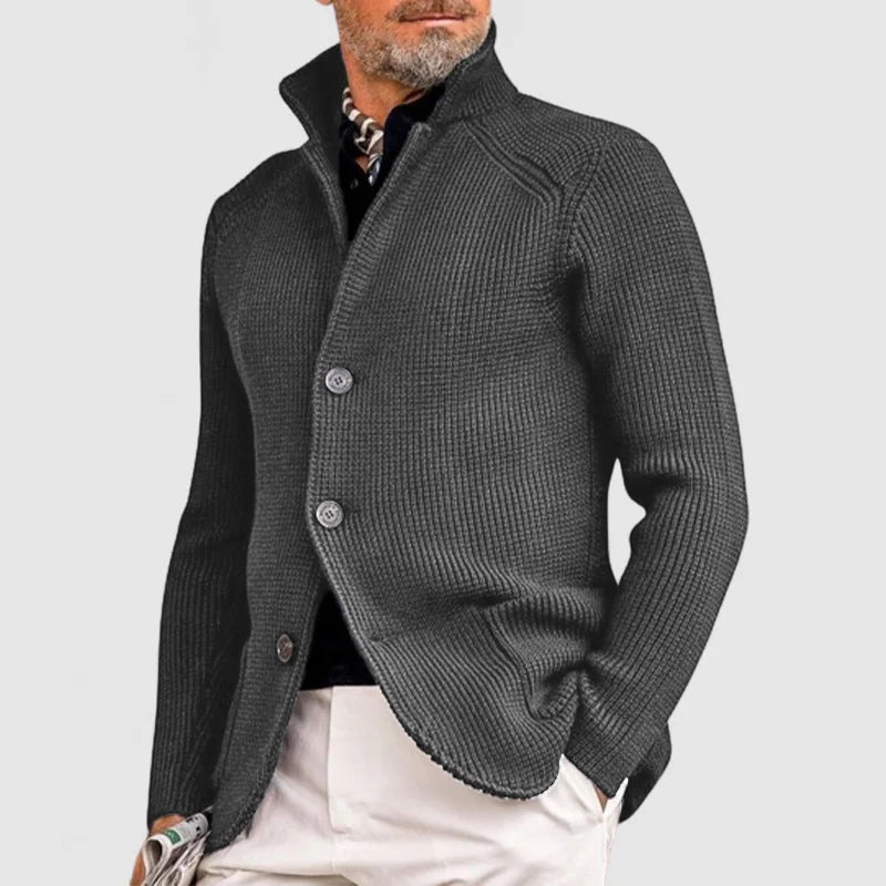 Homme portant un cardigan gris élégant, col relevé, sur chemise noire et pantalon beige, style mode masculine automne-hiver, look chic et moderne.