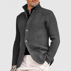 Homme portant un cardigan gris élégant, col relevé, sur chemise noire et pantalon beige, style mode masculine automne-hiver, look chic et moderne.