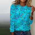 Femme portant un pull bleu à motifs floraux colorés, manches longues, col rond, avec un collier et une montre. Mode féminine décontractée.