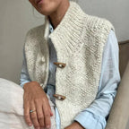 Gilet en laine tricoté à la main avec boutons en bois, porté sur une chemise bleue. Mode automne-hiver, style décontracté et élégant.