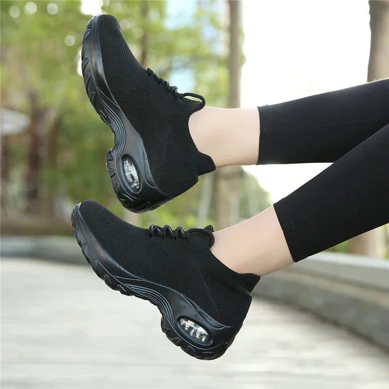 Chaussures de sport noires pour femmes avec semelle épaisse et coussin d'air, portées en extérieur. Confort, style, baskets tendance.