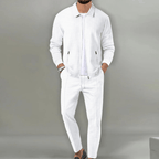 Homme en costume blanc élégant, veste et pantalon assortis, montre-bracelet noire, fond gris. Mode masculine, tenue chic, style moderne.