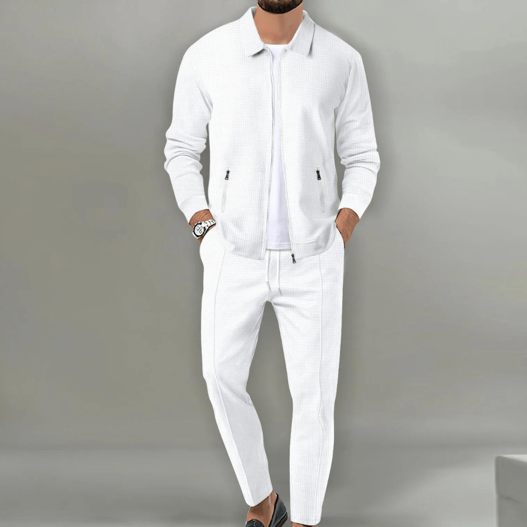 Homme en costume blanc élégant, veste et pantalon assortis, montre-bracelet noire, fond gris. Mode masculine, tenue chic, style moderne.
