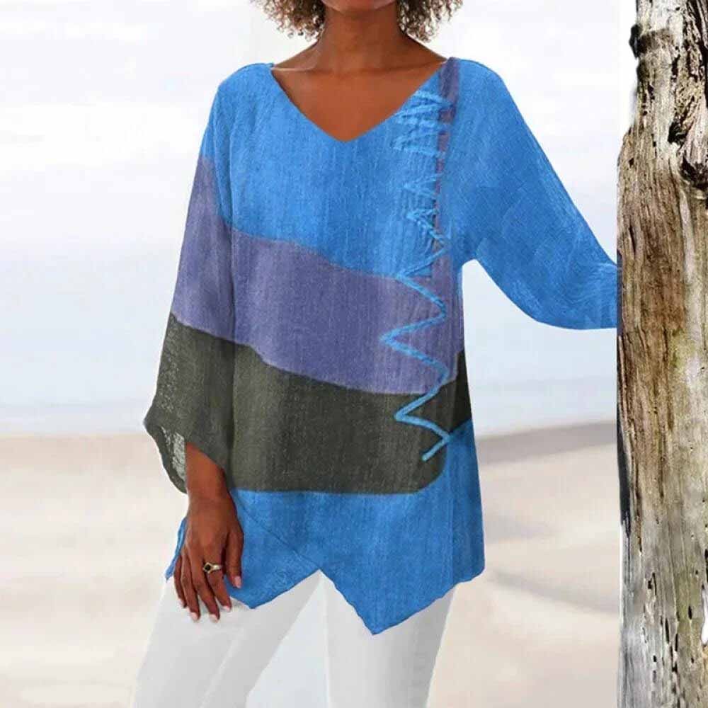 Femme portant une tunique bleue à motifs géométriques, manches trois-quarts, col en V, sur fond de plage. Mode estivale, tenue décontractée.
