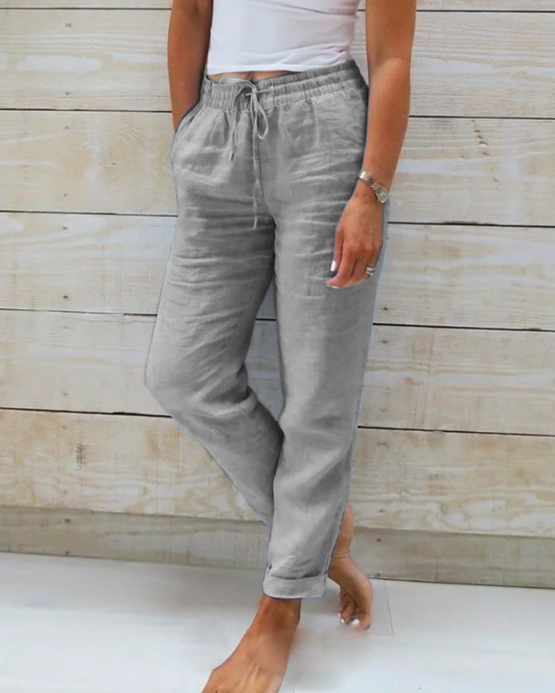 Pantalon en lin gris pour femme, taille élastique avec cordon, poches latérales, style décontracté, fond en bois clair.