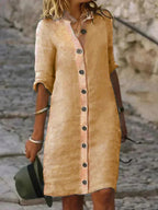 Robe chemise beige à manches longues, boutons décoratifs, portée par une femme sur un chemin pavé. Mode décontractée, style estival élégant.