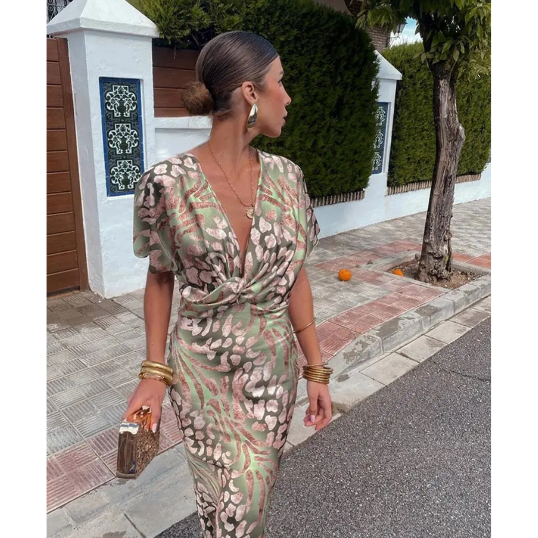 Robe élégante à motifs floraux, femme marchant sur un trottoir, accessoires dorés, sac à main chic, coiffure chignon, ambiance estivale.