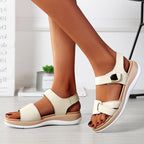 Sandales blanches pour femmes avec semelles compensées, design moderne et confortable, portées sur un sol en bois clair, style estival élégant.