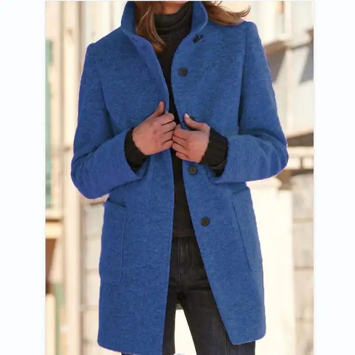 Femme portant un manteau bleu élégant, col relevé, sur un pull noir, en extérieur urbain. Mode automne-hiver, style chic et moderne.