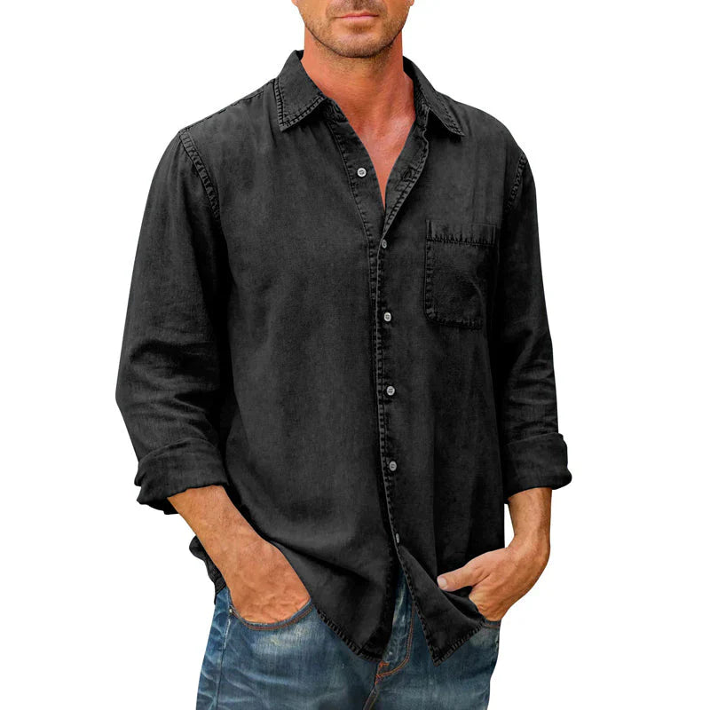 Homme portant une chemise noire en denim avec manches longues retroussées, poche poitrine, et jeans décontractés. Mode masculine, style casual chic.