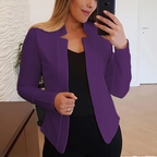 Femme en veste violette élégante prenant un selfie, intérieur moderne, mur texturé, tenue professionnelle, mode féminine, smartphone.