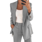 Femme en costume gris élégant, veste et pantalon assortis, tenant un smartphone. Mode professionnelle, tenue de bureau chic.