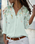 Femme portant une chemise verte à motifs floraux et oiseaux, manches longues, col ouvert, ceinture marron, style décontracté et élégant.