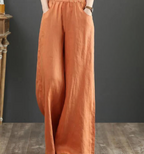 Pantalon large en lin orange pour femme, taille élastique, style décontracté, mode automne, sur fond gris et sol en bois.
