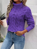 Femme portant un pull violet à col roulé torsadé, tenant un gobelet de café, posant contre un mur blanc. Mode automne, style décontracté.