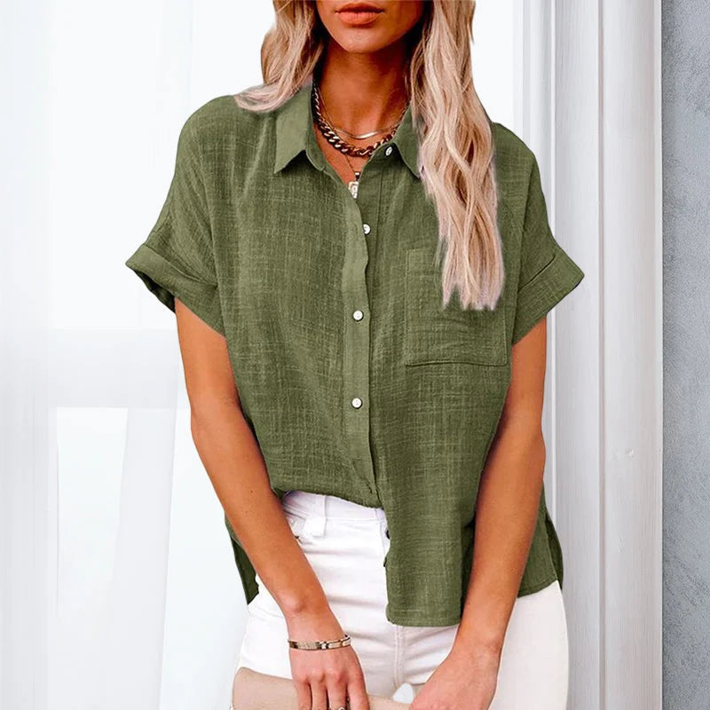 Femme portant une chemise en lin vert olive, manches courtes, col boutonné, associée à un pantalon blanc. Mode décontractée, tendance été.