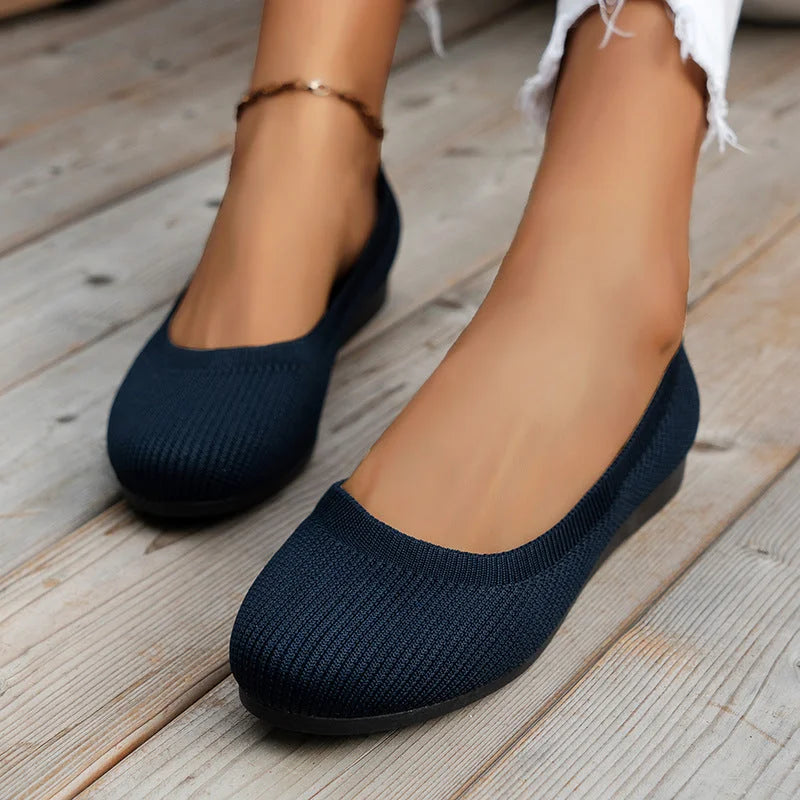 Chaussures ballerines bleu marine sur pieds féminins, posées sur un sol en bois. Mode décontractée, élégance, confort, style moderne.