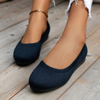 Chaussures ballerines bleu marine sur pieds féminins, posées sur un sol en bois. Mode décontractée, élégance, confort, style moderne.
