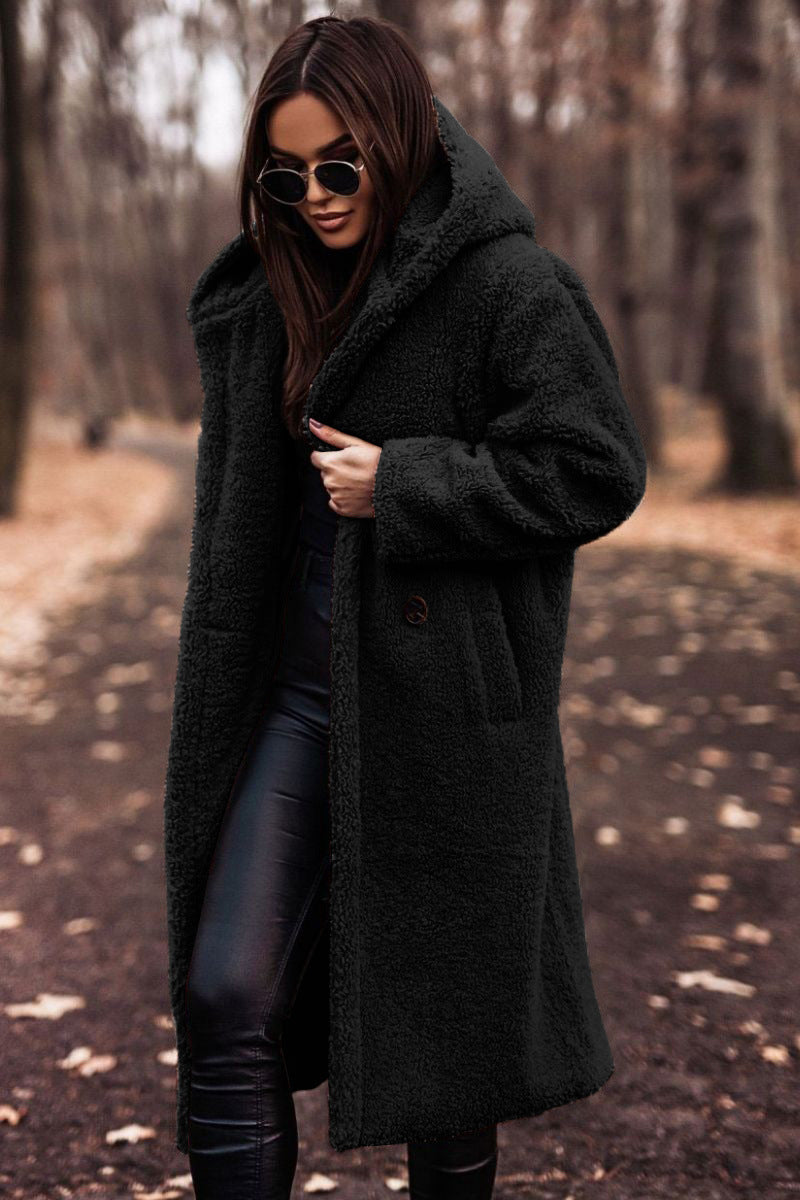 Femme portant un manteau en fausse fourrure noir, lunettes de soleil, marchant dans un parc automnal. Mode hiver, style élégant, tendance.