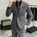 Homme en costume gris élégant, cravate noire, montre argentée, posant près d'une enceinte vintage et d'un portant à vêtements. Mode masculine chic.