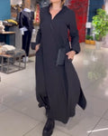 Robe longue noire élégante portée par une femme dans une boutique moderne, avec sac à bandoulière noir et bottes, mode chic et tendance.