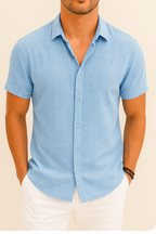 Homme portant une chemise bleue à manches courtes, col ouvert, avec un pantalon blanc. Mode masculine élégante, tenue estivale décontractée.