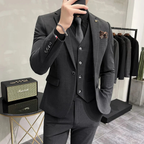 Homme en costume gris élégant, cravate noire, posant devant un amplificateur et un portant de vêtements. Mode masculine, style formel, boutique.