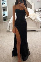 Robe de soirée noire élégante avec fente haute, portée par une femme dans une chambre moderne. Mode féminine, tenue de soirée chic.