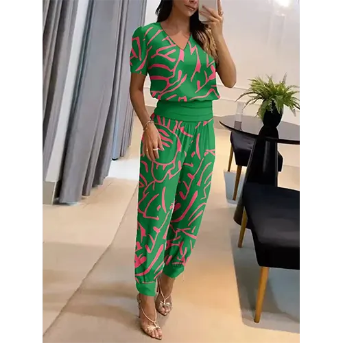 Femme portant une combinaison verte à motifs roses, posant devant un miroir. Mode élégante, tenue d'été, style décontracté chic.