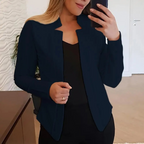 Femme en veste noire élégante prenant un selfie dans un intérieur moderne, tenue professionnelle, mode féminine, style chic et contemporain.