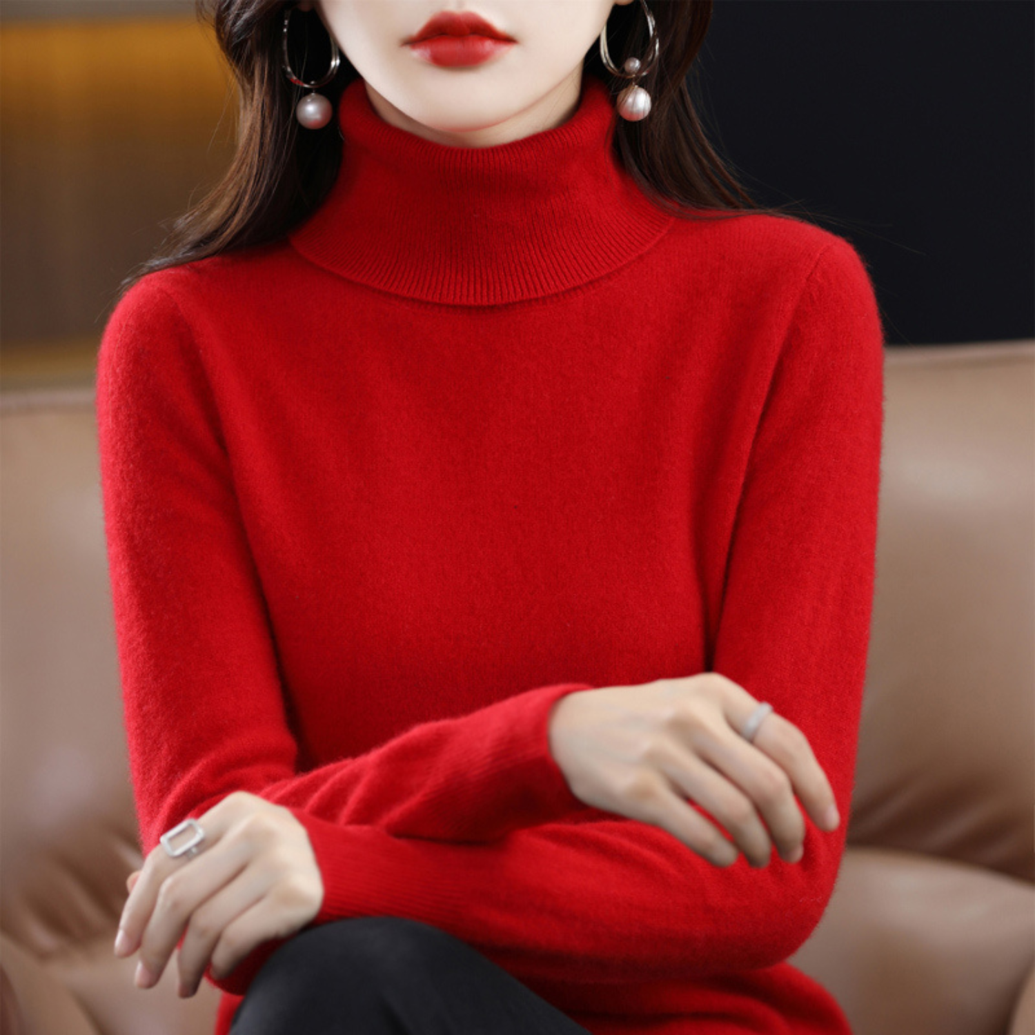 Femme en pull rouge à col roulé, assise sur un canapé, portant des boucles d'oreilles perle et rouge à lèvres assorti. Mode élégante et chic.