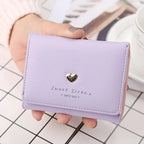 Portefeuille violet en cuir avec un motif de cœur argenté, posé sur une table à carreaux. Accessoire mode élégant pour femmes, tendance et pratique.