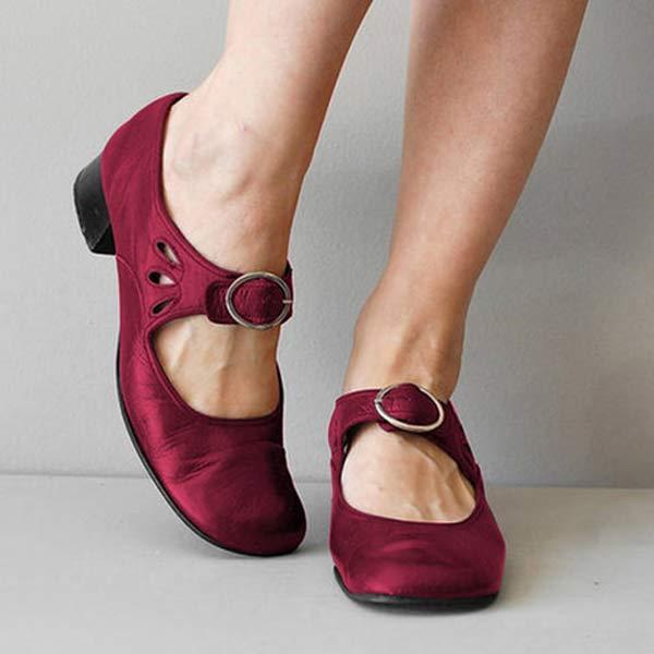 Chaussures rouges à talons bas avec boucle, portées par une personne debout. Design élégant et confortable, idéal pour mode féminine et occasions formelles.