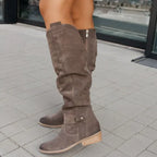 Bottes hautes en daim marron pour femme, avec talon bas, sur trottoir pavé. Mode automne, chaussures élégantes et confortables.