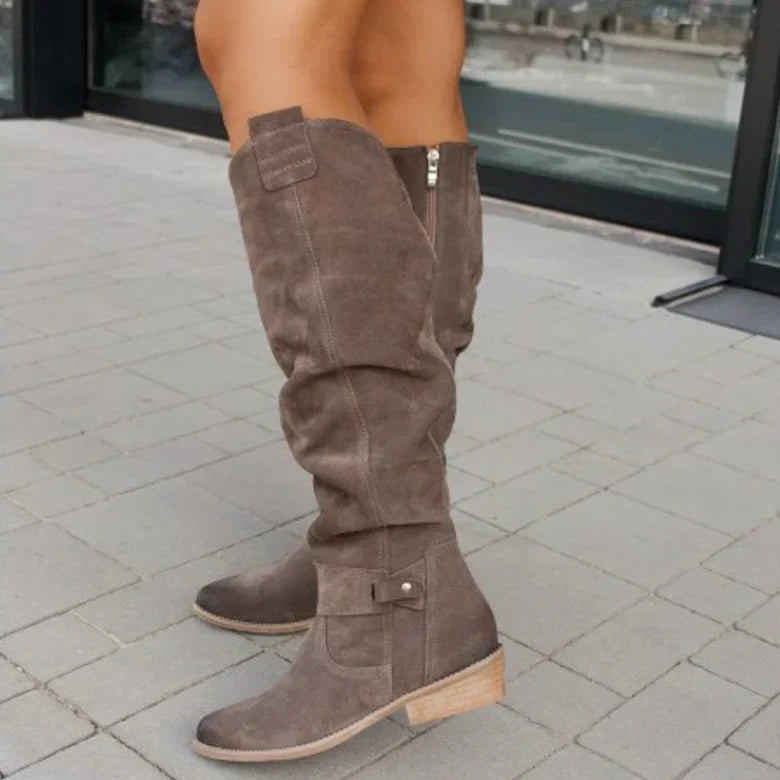 Bottes hautes en daim marron pour femme, avec talon bas, sur trottoir pavé. Mode automne, chaussures élégantes et confortables.