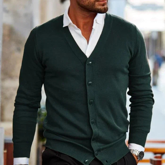 Homme portant un cardigan vert foncé élégant sur chemise blanche, style mode masculine chic, rue urbaine.