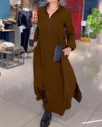 Robe longue marron élégante portée par une femme dans une boutique de mode, avec sac noir en bandoulière et bottes noires, intérieur moderne.