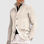 Homme portant un cardigan beige élégant, col relevé, boutons visibles, sur chemise noire et pantalon clair. Mode masculine chic et moderne.