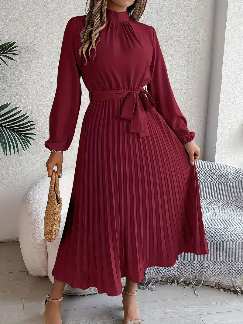 Robe longue plissée bordeaux avec ceinture, manches longues, tenue élégante pour femme, accessoire sac en paille, intérieur moderne.