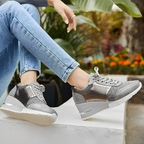 Baskets argentées pour femme avec semelle compensée, portées avec un jean bleu clair, posées sur un muret, fond de plantes et fleurs colorées.