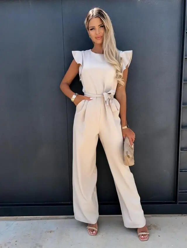 Femme en combinaison beige élégante, posant devant un mur noir. Mode féminine chic, tenue d'été tendance, style moderne et sophistiqué.