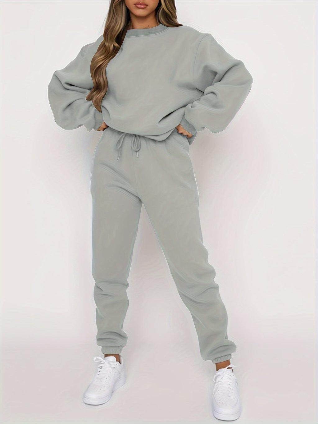 Femme portant un ensemble de survêtement gris, composé d'un sweat ample et d'un pantalon ajusté, avec des baskets blanches. Mode décontractée tendance.