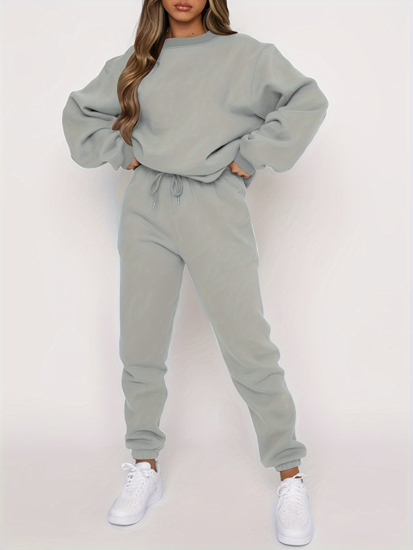 Femme portant un ensemble de survêtement gris, composé d'un sweat ample et d'un pantalon ajusté, avec des baskets blanches. Mode décontractée tendance.