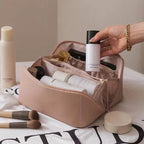 Trousse de maquillage rose ouverte avec produits de beauté, pinceaux et flacons. Main tenant un flacon blanc. Accessoires cosmétiques organisés.