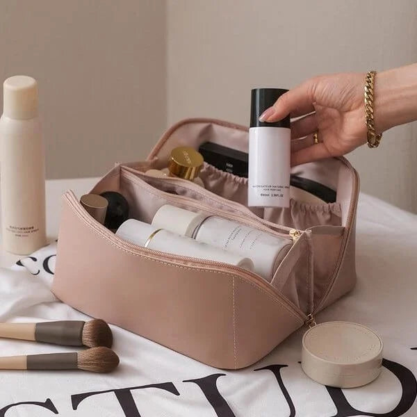 Trousse de maquillage rose ouverte avec produits de beauté, pinceaux et flacons. Main tenant un flacon blanc. Accessoires cosmétiques organisés.